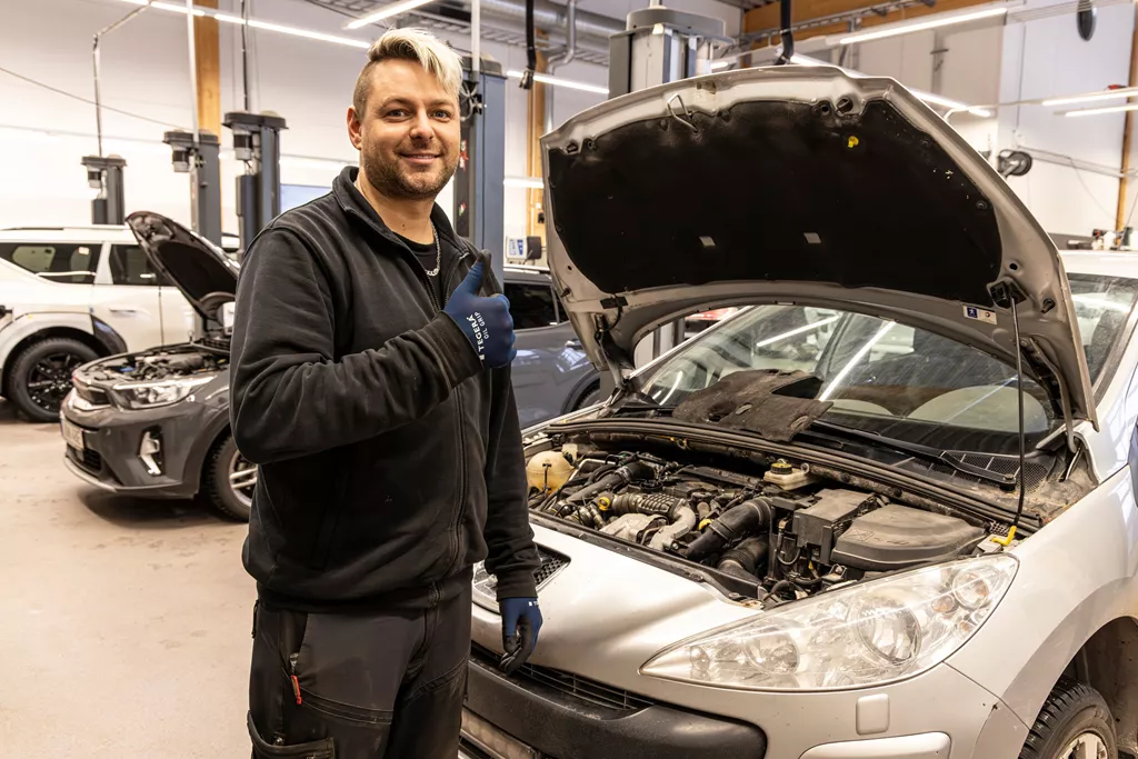Automotive technician wearing TEGERA Oil Grip 8850 safety gloves while servicing a car in a workshop.