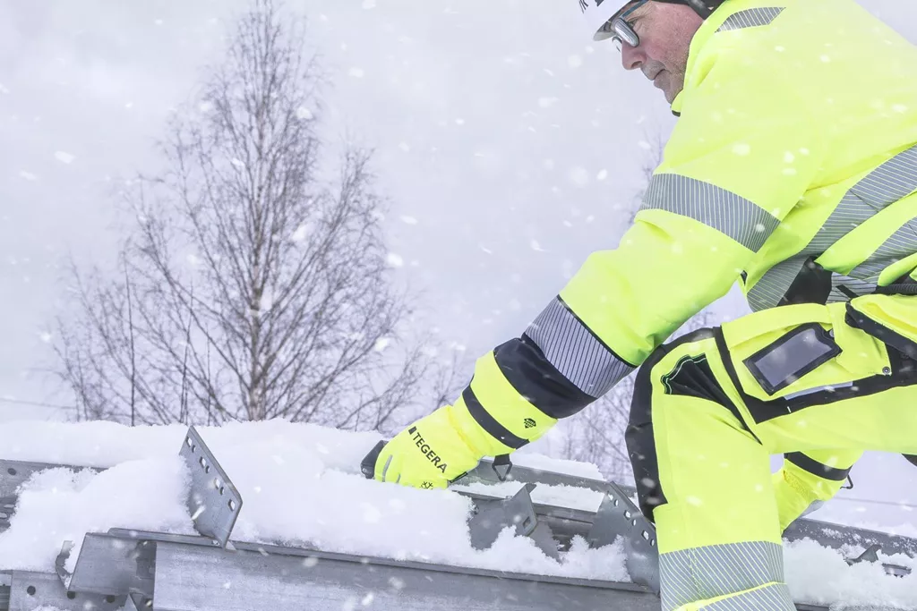 Worker wearing TEGERA 6299 winter gloves handling snow-covered metal in cold conditions.